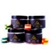 Four jars of Delta Remedy ring gummies in Watermelon, Apple, Blue Raspberry, and Peach flavors, stacked and surrounded by stacks of their respective gummies