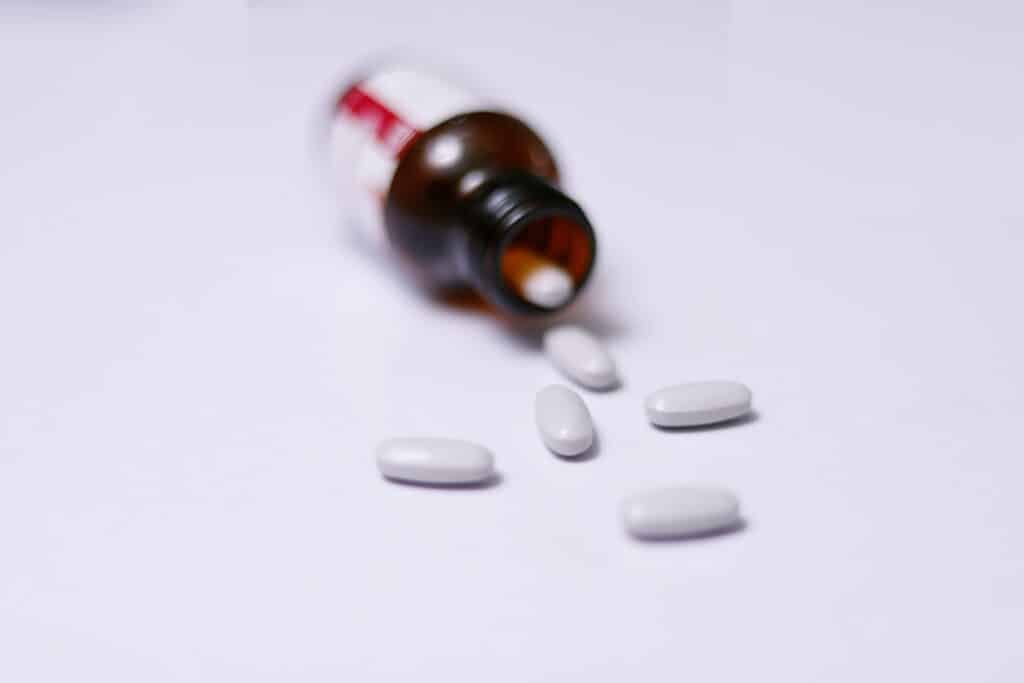 White tablets spilled from a brown medicine bottle on a white background, symbolizing pharmaceutical or supplement use.